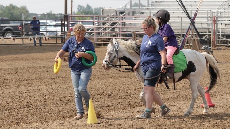 CHAPS volunteers assisting a young rider on a paint horse using cones and colored rings